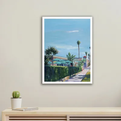 A framed giclée print of a palm-lined street on a gallery wall